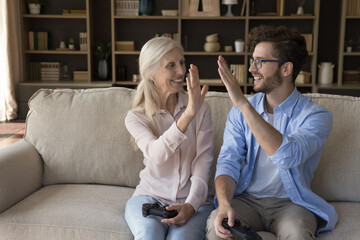 Intergenerational dream team. Cheerful gen z man win video game challenge together with excited older granny sharing high five to celebrate success with joyful grandparent holding gamepad. Copy space