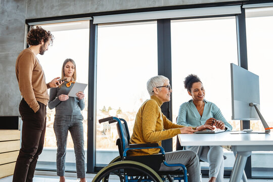 The image includes a person using a wheelchair, depicting inclusivity and teamwork in modern office