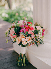 Flower bouquet showcasing pink and peach roses with greenery on a sunny day in a garden setting