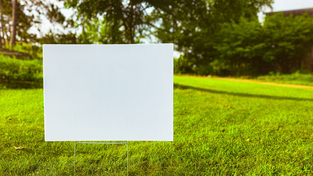 a blank white lawn sign in a grass area with copy space. room for text to announce events, advertisements, real estate, or other creative projects. wide background or banner. sunny outdoor landscape.