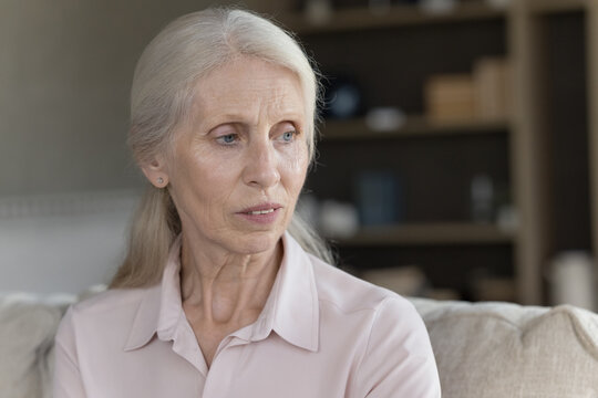 Sadness of aging. Head shot portrait unhappy older woman sit on couch lost in unpleasant thoughts ponder retirement difficulties health problems mourning lost youth feel lonely forgotten. Copy space - Powered by Adobe