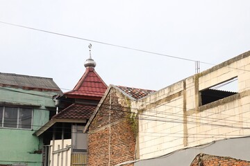 Urban architectural old building with exposed red brick walls, weathered white concrete, and a green painted structure with rusty roof edges. The standout detail is a small mosque dome.