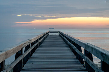 Fototapeta premium Luc-Sur-Mer, France - 08 07 2025: View of the wooden pier in front of the sea named Fisherman's Pier at sunrise and Le Havre far away