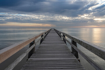 Obraz premium Luc-Sur-Mer, France - 08 07 2025: View of the wooden pier in front of the sea named Fisherman's Pier at sunrise and Le Havre far away