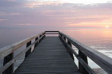 Fototapeta premium Luc-Sur-Mer, France - 08 07 2025: View of the wooden pier in front of the sea named Fisherman's Pier at sunrise and Le Havre far away
