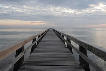 Obraz premium Luc-Sur-Mer, France - 08 07 2025: View of the wooden pier in front of the sea named Fisherman's Pier at sunrise and Le Havre far away