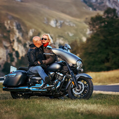 Obraz premium Romantic couple enjoying a tender moment on a cruiser motorcycle in the mountains at sunset, symbolizing love, freedom, and adventure travel lifestyle