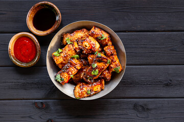 Asian roasted pork with sriracha sauce, hot pepper and sesame. Pieces of meat fried in soy sauce on black wooden background top view copy space for text