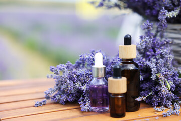 Beautiful lavender flowers and bottles of essential oils on wooden table in field, closeup. Space for text