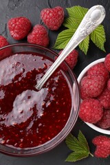Sweet raspberry jam in glass bowl and berries on gray textured table, flat lay