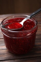 Sweet raspberry jam in glass jar and spoon on wooden table, closeup