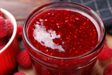 Sweet raspberry jam in glass jar and berries on table, closeup
