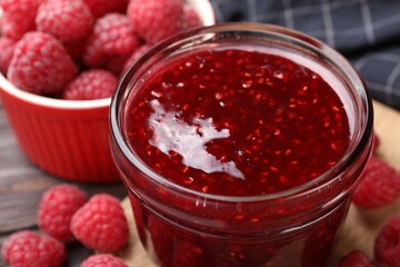 Sweet raspberry jam in glass jar and berries on table, closeup