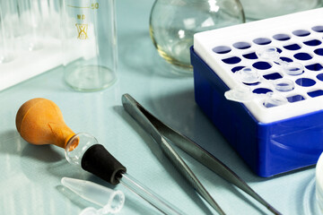 Laboratory equipment including test tubes, pipettes, and tweezers on a glass surface. 