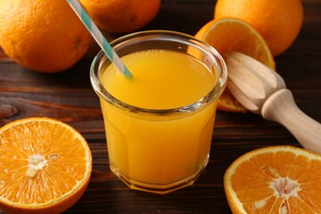Fresh orange juice in glass, fruits and juicer on wooden table, closeup