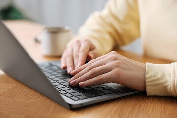 Copywriter using laptop at wooden table indoors, closeup