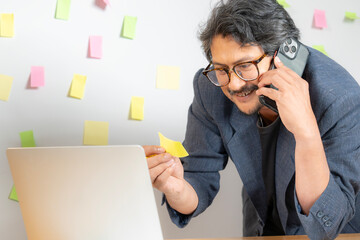 Conceptual image of a young businessman brainstorming and writing business ideas on sticky notes, placing them on the wall for planning and strategy development