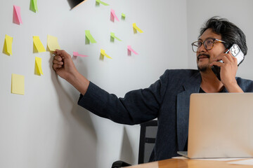 Conceptual image of a young businessman brainstorming and writing business ideas on sticky notes, placing them on the wall for planning and strategy development