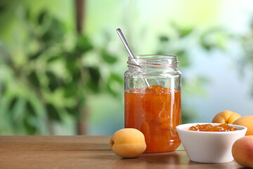 Tasty apricot jam and fresh fruits on wooden table against blurred background, closeup. Space for text