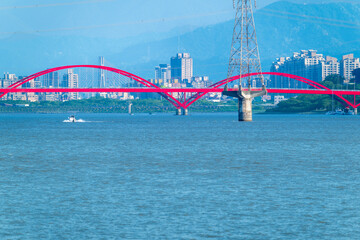 Obraz premium Stunning view of the pink bridge spanning the Danshui River in Taiwan at twilight, with calm waters and distant mountains. Shot on April 29, 2025.