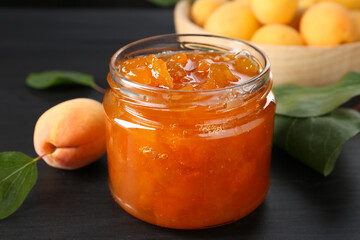 Tasty apricot jam and fresh fruits on black wooden table, closeup
