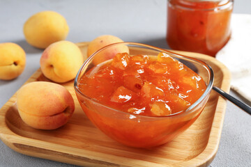 Tasty apricot jam and fresh fruits on light grey table, closeup