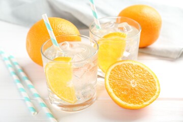 Sparkling water with orange slices in glasses and fresh fruits on white wooden table, closeup