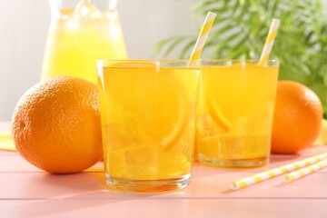 Refreshing soda water with orange slices in glasses, jug and fresh fruits on pink wooden table, closeup