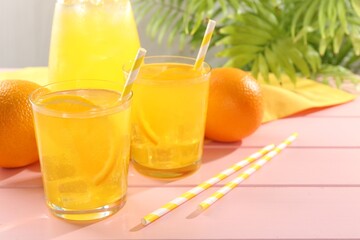 Refreshing soda water with orange slices in glasses, jug and fresh fruits on pink wooden table, closeup