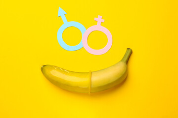 Sex education. Banana with condom, paper female and male gender symbols on yellow background, flat...