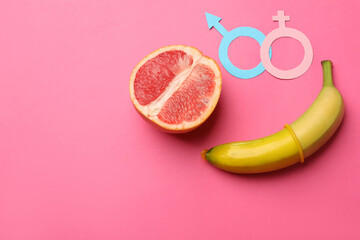 Sex education. Banana with condom, grapefruit, paper female and male gender symbols on pink...