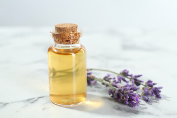 Aromatic essential oil in bottle and lavender flowers on white marble table, closeup