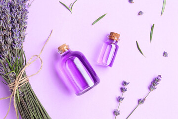 Aromatic essential oil in bottles and lavender flowers on violet background, flat lay