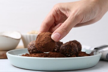 Woman making homemade candies with cocoa powder at white table, closeup