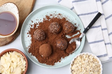Delicious homemade candies with cocoa powder and other ingredients on white tiled table, flat lay