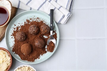 Delicious homemade candies with cocoa powder and other ingredients on white tiled table, flat lay. Space for text