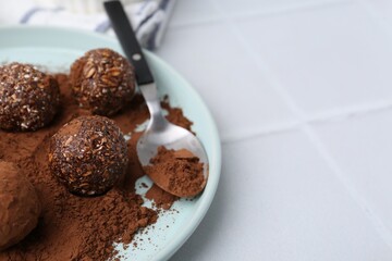 Delicious homemade candies with cocoa powder on white tiled table, closeup. Space for text