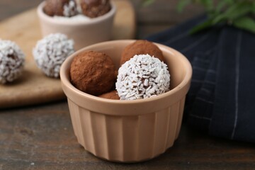 Delicious homemade candies with cocoa powder and coconut flakes in bowl on wooden table, closeup