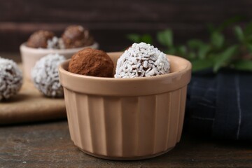 Delicious homemade candies with cocoa powder and coconut flakes in bowl on wooden table, closeup
