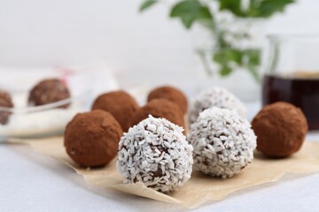 Delicious homemade candies with cocoa powder and coconut flakes on light table, closeup
