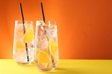 Refreshing soda water with orange slices and ice cubes in glasses on yellow table against orange background. Space for text