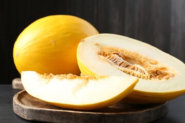 Cut and whole ripe melons on black wooden table, closeup