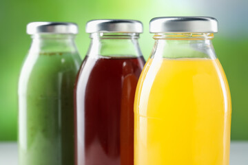 Tasty juices in glass bottles on blurred green background, closeup
