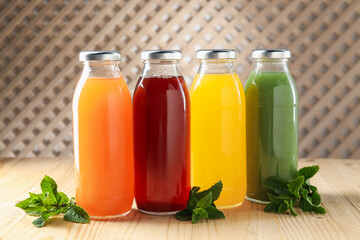 Tasty juices in glass bottles and mint on wooden table indoors, closeup