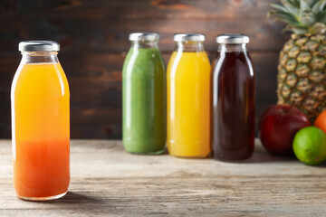 Tasty juices in glass bottles and fresh ingredients on wooden table against brown background, closeup