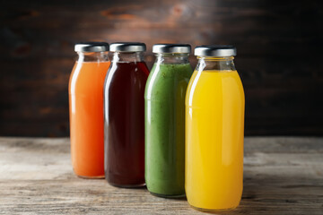 Tasty juices in glass bottles on wooden table against brown background, closeup
