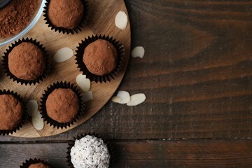 Delicious homemade candies with cocoa powder and coconut flakes on wooden table, flat lay. Space for text
