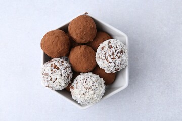 Delicious homemade candies with cocoa powder and coconut flakes in bowl on white table, top view