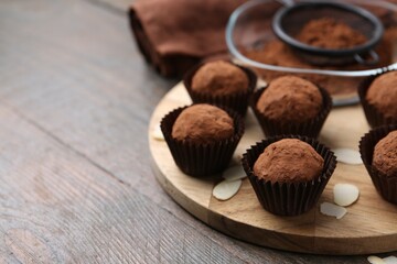 Delicious homemade candies powdered with cocoa on wooden table, closeup. Space for text