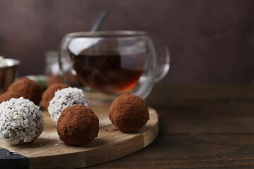 Delicious homemade candies with cocoa powder, coconut flakes and tea on wooden table, closeup. Space for text